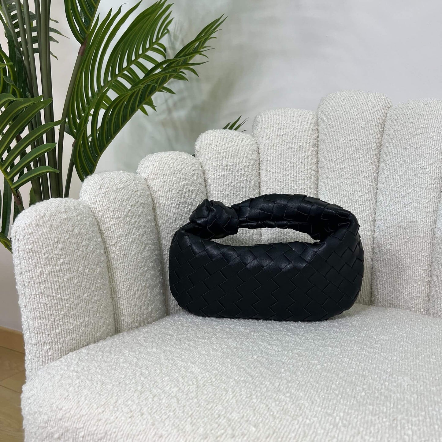 Borsa nera intrecciata con manico a nodo, modello Knot ÈCLAT, fotografata su poltrona elegante