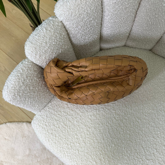 Vista dall’alto della borsa Knot color cammello intrecciata, appoggiata su poltrona chiara elegante.