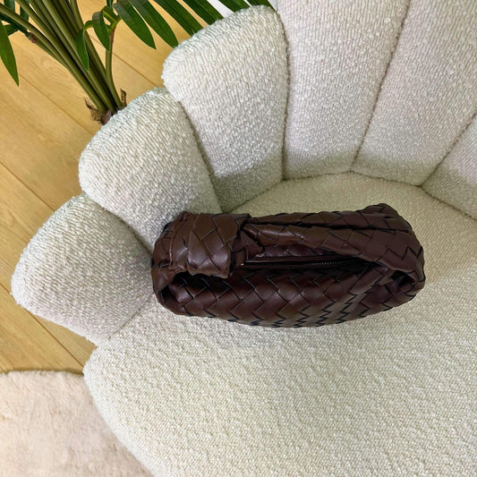 Vista dall’alto della borsa Knot color marrone fondente intrecciata, appoggiata su poltrona chiara elegante.