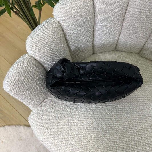 Vista dall’alto della borsa Knot nera intrecciata, appoggiata su poltrona chiara elegante