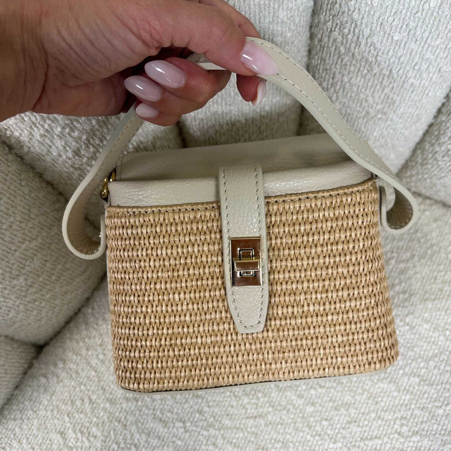 Borsa ÈCLAT Alma in rafia e pelle color avorio, beige, vista con manico corto in mano su sfondo neutro