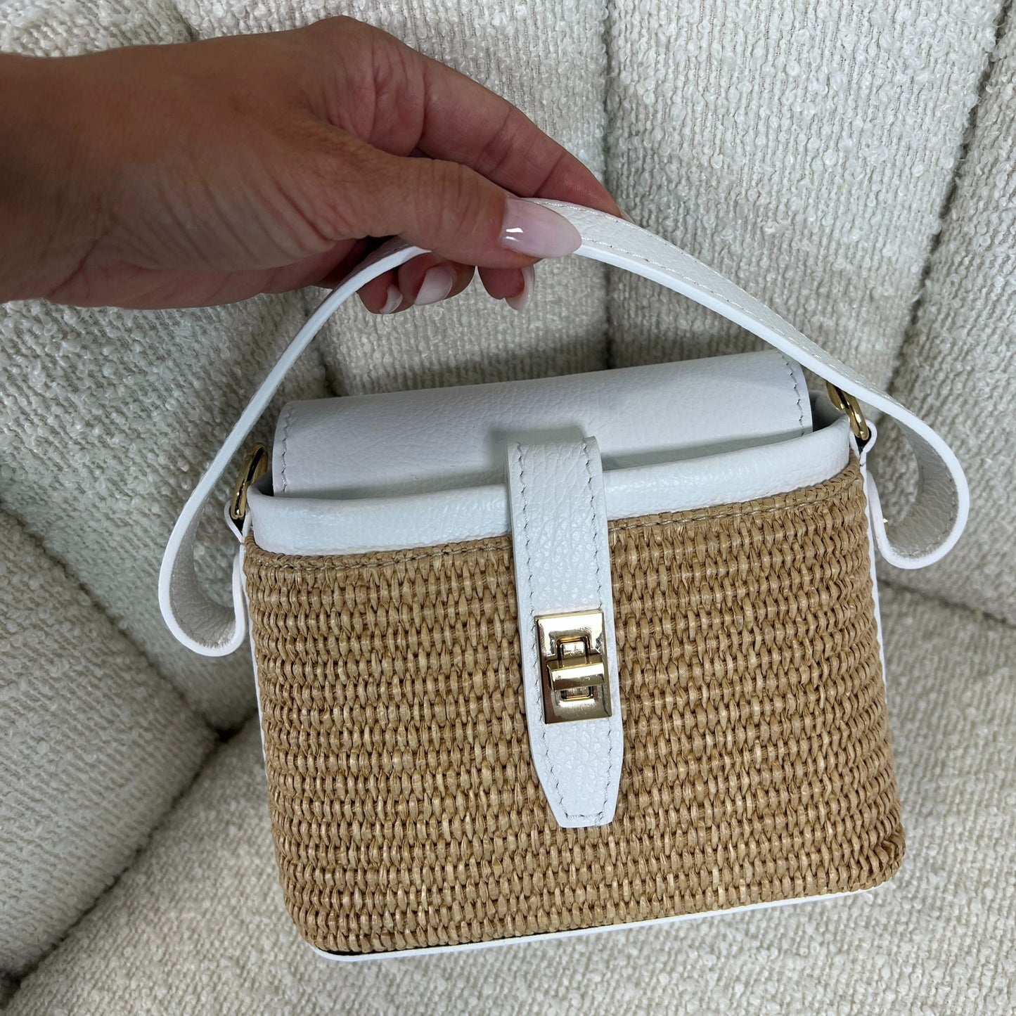Borsa ÈCLAT Alma in rafia e pelle color bianco, vista con manico corto in mano su sfondo neutro