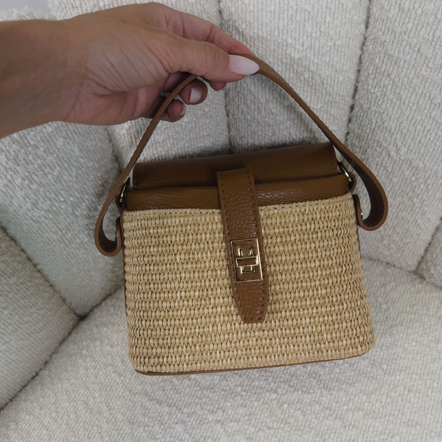 Borsa ÈCLAT Alma in rafia e pelle color cognac, vista con manico corto in mano su sfondo neutro