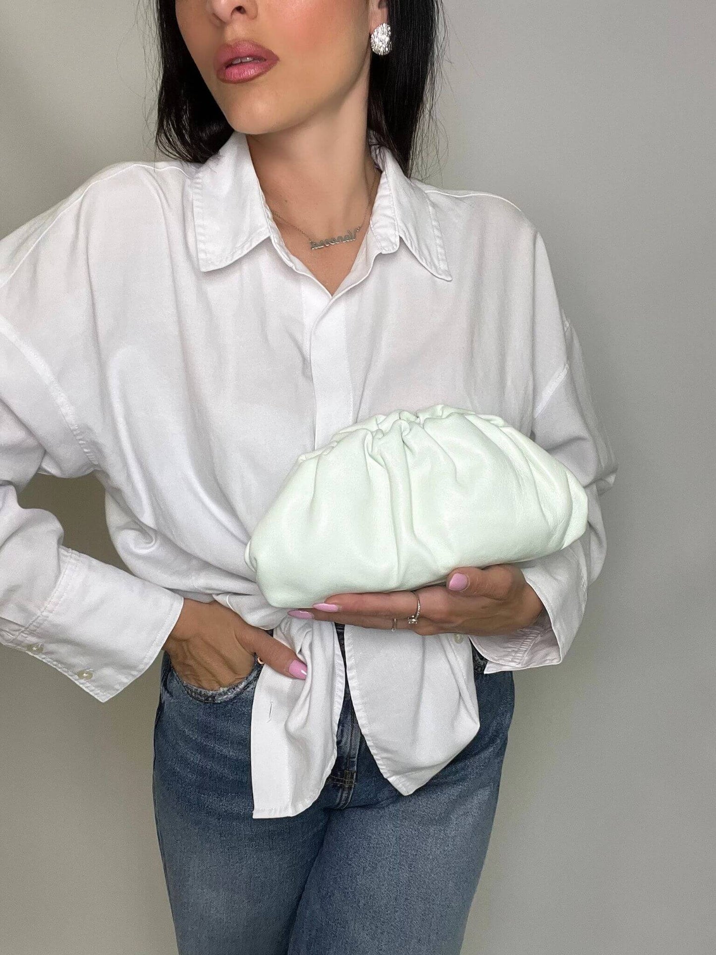 Modella con camicia bianca e jeans che indossa mini pouch menta glaciale ÉCLAT Bags in stile Bottega Veneta, look elegante e raffinato