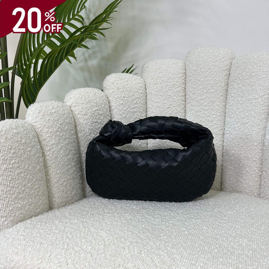 
Borsa color nero black intrecciata con manico a nodo, modello Knot ÈCLAT, fotografata su poltrona elegante. simile alla jodie di bottega veneta