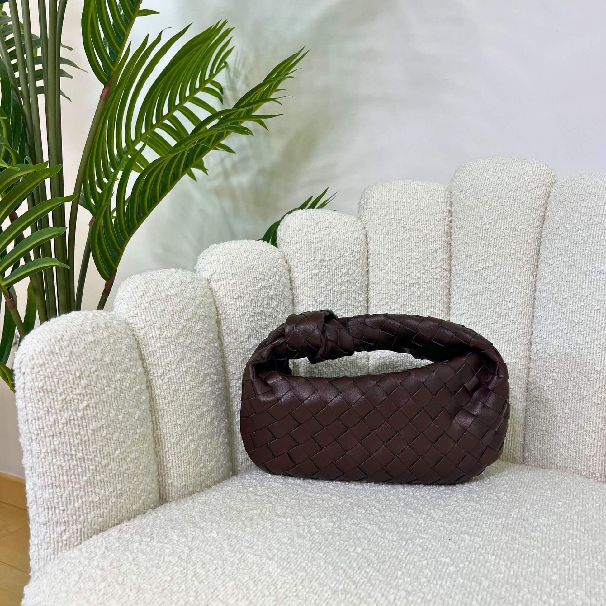 Borsa color marrone fondente  intrecciata con manico a nodo, modello Knot ÈCLAT, fotografata su poltrona elegante