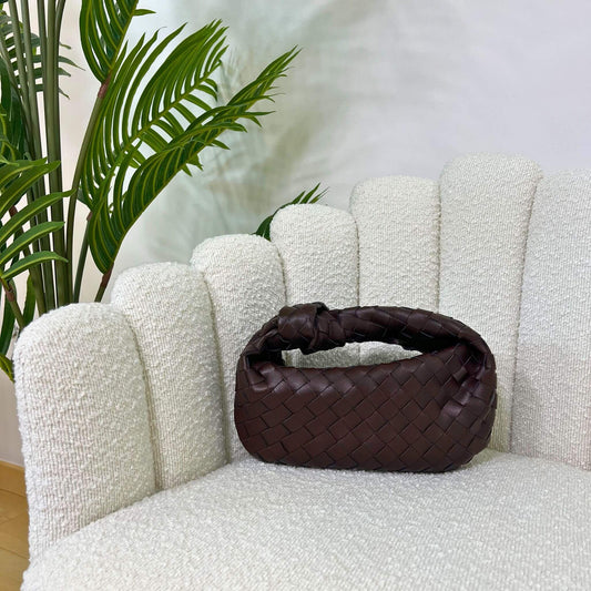 Borsa color marrone fondente  intrecciata con manico a nodo, modello Knot ÈCLAT, fotografata su poltrona elegante